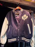 Front view of jacket on hanger showing wool body, leather sleeves, patch, snap front