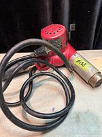 Heat gun coiled with cord showing red body and vented top