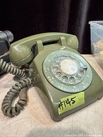 Oblique view of green rotary telephone showing handset, body and coiled cord