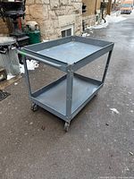 Full view of gray metal utility cart showing both shelves, casters and handle