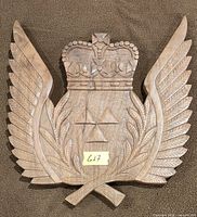 Front view of carved wooden plaque showing crown, wings, laurel branches and triangular insignia