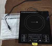 Top view of Kuraidori induction cooktop beside sealed user manual
