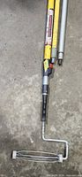 Three extension poles, one with paint roller frame, lying on concrete