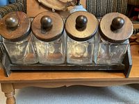 Front view of four glass canisters with wood lids in rack