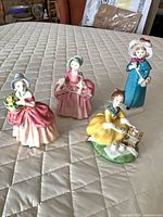 Group shot of all four Royal Doulton figurines on quilted surface