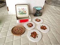 Assorted coasters laid out including Pimpernel box, ceramic fruit, scenic, wooden
