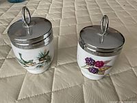 Both egg coddlers with lids on showing decorations