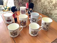 Group view of seven commemorative mugs and two guard figurines