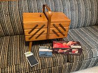 Closed wooden sewing box with handle and tripod legs; handheld sewing machine box, denim patches, small notion pack visible