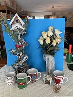 Group view of birdhouse décor, artificial roses, four mugs and music box