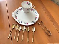 Overview showing plate, teacup, six spoons and tongs