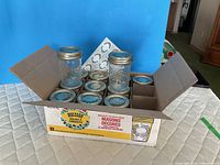 Open box showing multiple mason jars, one jar upright displaying embossed design and lid