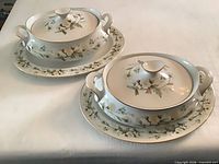 Two covered serving bowls each on matching oval platter