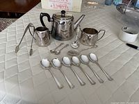 Group shot of teapot, creamer, sugar bowl, tongs, assorted spoons