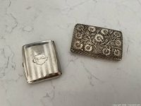 Both cigarette cases closed, showing size and design contrast