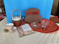 Group shot of entire lot showing teapot, teacup and saucer, tea cosy, placemats, glass sugar and creamer, spoon, pig figurine, spice mat