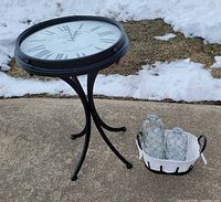 Full view of clock-top side table beside basket with two bottles