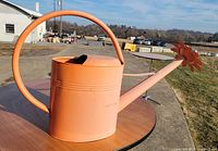 Side view of peach metal watering can on table showing full profile and handle