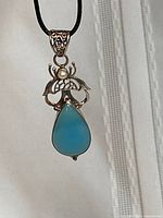 Front view of pendant showing blue chalcedony stone, faux pearl, and silver setting on black cord