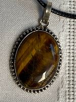 Close-up of oval tiger eye pendant in sterling silver bezel on black cord