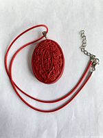 Front view of red carved oval cinnabar pendant on red cord