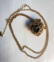 Necklace laid flat showing heart locket, chain, lobster clasp, lava stone visible