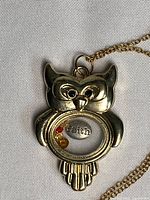 Front view of owl locket showing glass window, "faith" charm and beads