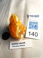 Front view of orange calcite specimen beside scale tag