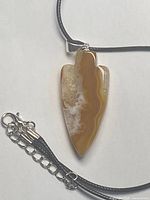 Front view of agate arrowhead pendant on cord showing color banding and clasp