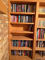 Five shelves of assorted fiction and thriller books on built-in light wood shelving