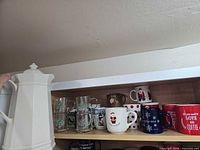 Carafe and multiple holiday mugs on shelf