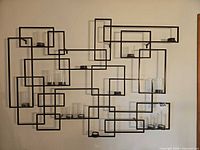 Full view of geometric metal wall candle holder mounted on wall with glass cylinders inserted