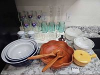 Entire lot on countertop showing glassware, mixing bowls, CorningWare dishes, wooden salad set, yellow casserole, candlesticks and candle holder
