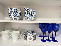 Cabinet view showing stacked bowls, mugs, plates, and blue wine glasses
