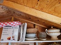 Shelf view showing boxed Cuisinart hand blender, ceramic plates, glass bowls, wicker tray, ceramic tureen