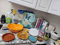 Countertop view showing ceramic bowls, cleaning sprays, reusable bag, cookbooks