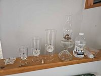 Full lot showing three glass cylinder lamps, starfish figurine, brass tool, brass snuffer, vintage table oil lamp, lamp oil bottle, and funnel kit