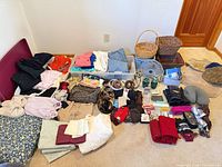 Full lot layout showing clothing stacks, bedding, storage bin and variety of accessories on floor