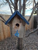 Weathered wood birdhouse with blue roof hanging in tree