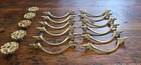 Full lot: 12 curved pulls and 5 floral knobs on wood surface