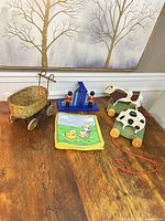 All items grouped on table: wicker wagon, two cow pull toys, soldier bookends, cloth book