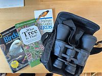 Binoculars in carrying case beside three field guide books