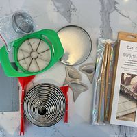 All items laid out: sushi kit box, nested cutters, bench scraper, apple slicer, Polygon spoons