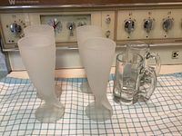 Four frosted footed beer glasses and two clear beer mugs on countertop