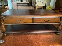 Front view of coffee table showing two drawers, lower shelf, carved legs
