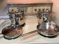 Group shot of two sauté pans and two stock pots with steamer inserts and lids on stovetop