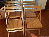 Front view of four matching wooden folding chairs showing slatted seats and backs