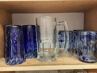 Group of eight blue swirl glass tumblers and one clear beer mug on shelf