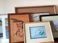 Group of framed and loose artworks leaning against wall
