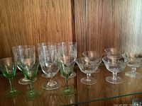 All 12 etched glasses arranged on shelf showing mix of green and clear stems and etched pattern